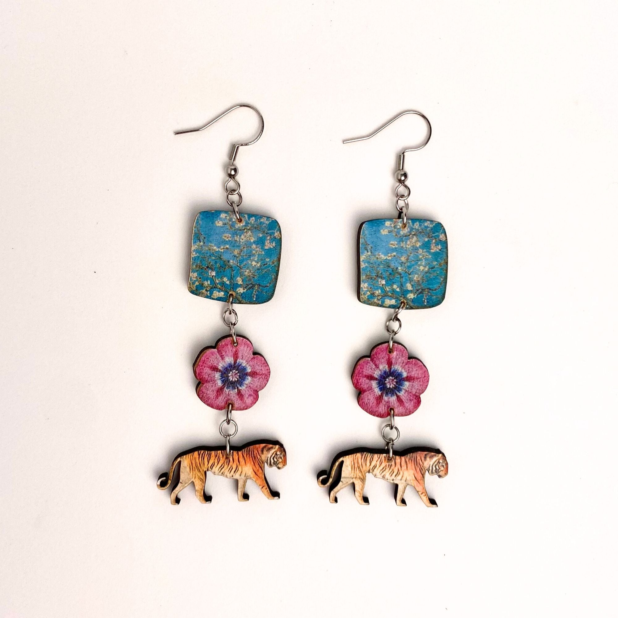Earrings with blue square pendants, pink floral charms, and tiger figures on a white background
